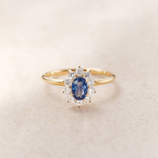 A Yellow Gold halo ring featuring an oval-cut, deep blue sapphire center stone secured by four golden prongs.