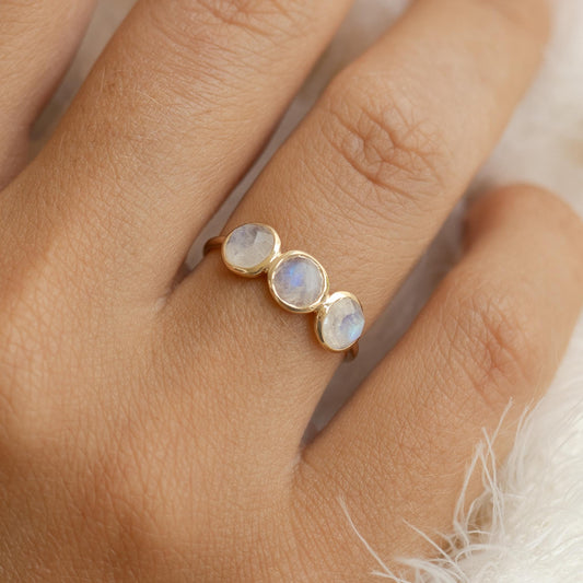 Close-up of hand wearing the Moonstone Ring 14k Gold - Elisa with three iridescent moonstones on a soft background
