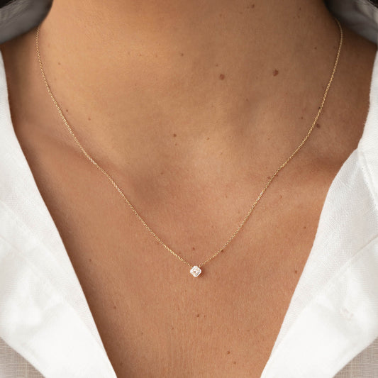 Close-up of a delicate Gold chain necklace with a small asscher-cut clear gemstone pendant, worn with a white V-neck blouse.