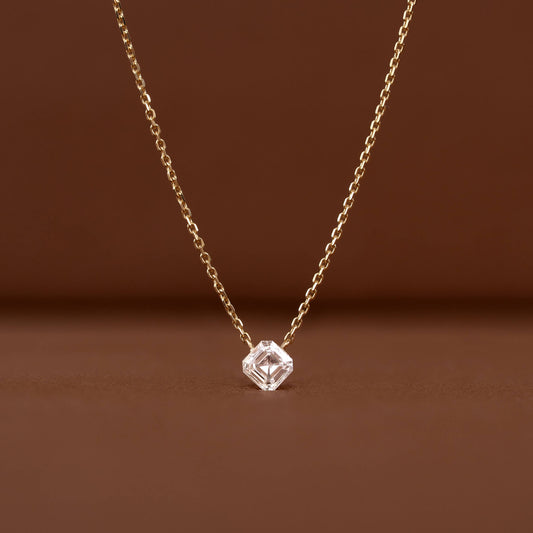 Close-up of a delicate Gold chain necklace featuring a clear asscher-cut gemstone pendant against a warm brown background.