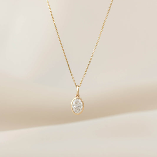 Yellow Gold necklace with a polished oval shaped pendant, displayed on a delicate chain against a soft neutral background.