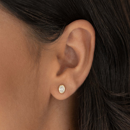 Close-up of a woman’s ear wearing an oval diamond stud earring set in a delicate Yellow Gold bezel.