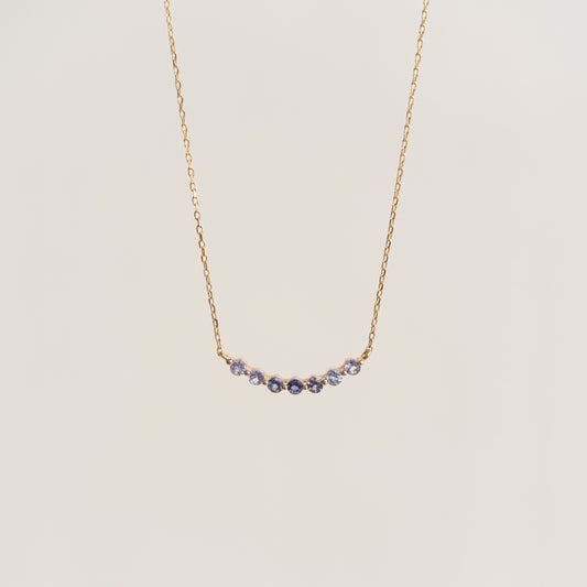 Close-up of December Birthstone Necklace 14k Gold - Ombre Cordierite with delicate blue-purple gemstones on thin gold chain on beige background