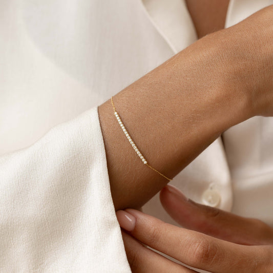 Close-up of a woman's wrist wearing the Diamond Curved Bar Bracelet 14k Gold - Vivienne with a white sleeve background