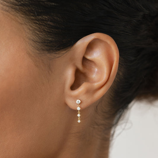 Close-up of a woman wearing Diamond Drop Earrings 14k Gold - Helmi featuring four diamonds on a delicate gold chain