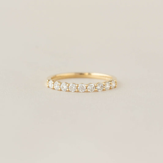 A delicate Gold band with round, sparkling diamonds set in a row, displayed on a light beige background, conveying elegance and simplicity.