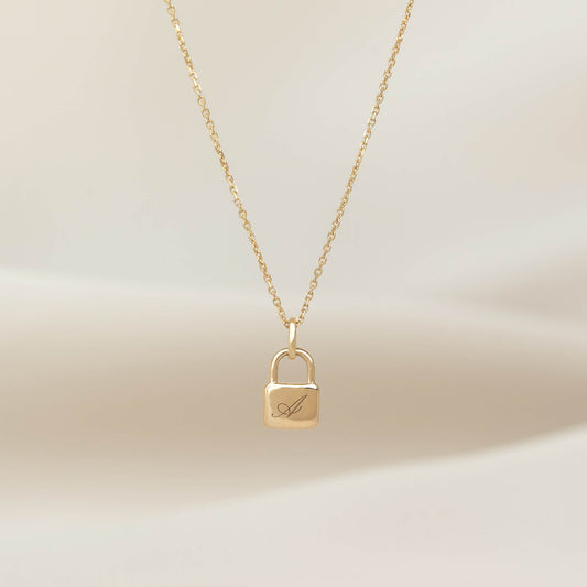 Yellow Gold necklace featuring a padlock-shaped pendant with an engraved letter “A,” displayed on a delicate chain against a soft neutral background.