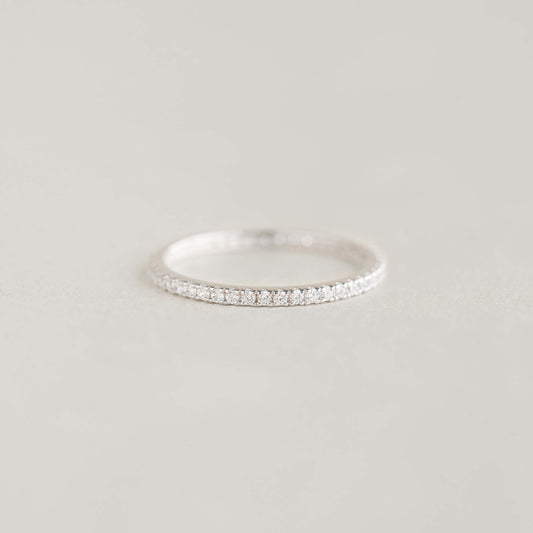 A delicate White Gold eternity ring adorned with small diamonds, elegantly placed on a soft, light gray surface, conveying a sense of simplicity and elegance.