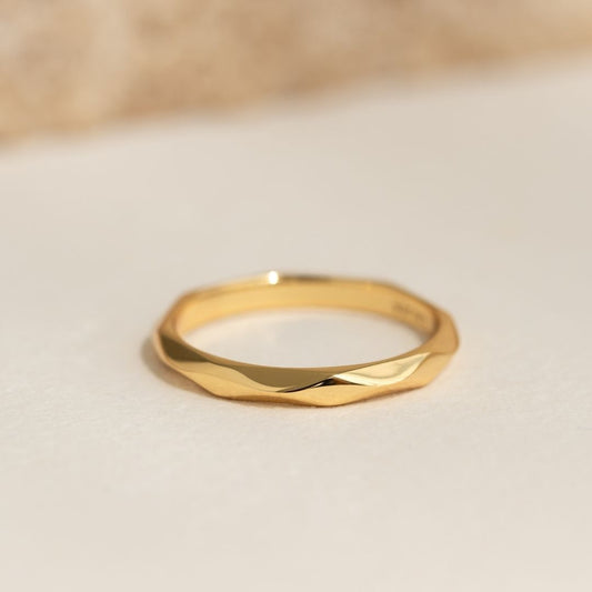 Close-up of a gold vermeil Faceted Ring - Rikka with a geometric wide band and faceted surface on a neutral background