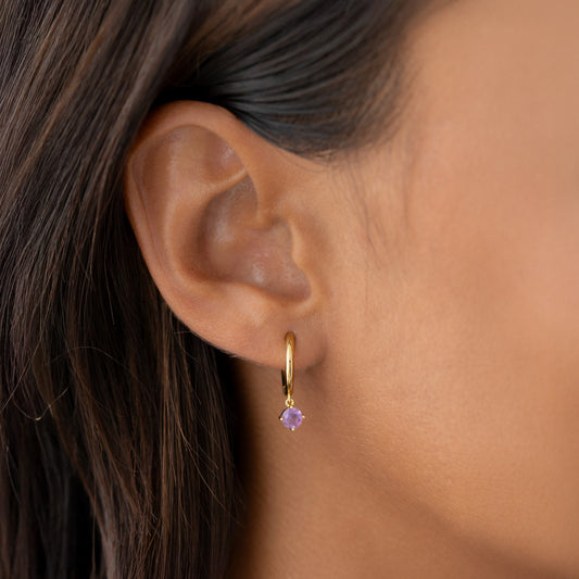 Close-up of an ear wearing February Birthstone Drop Huggie Earrings - Amethyst with gold vermeil and purple gemstone