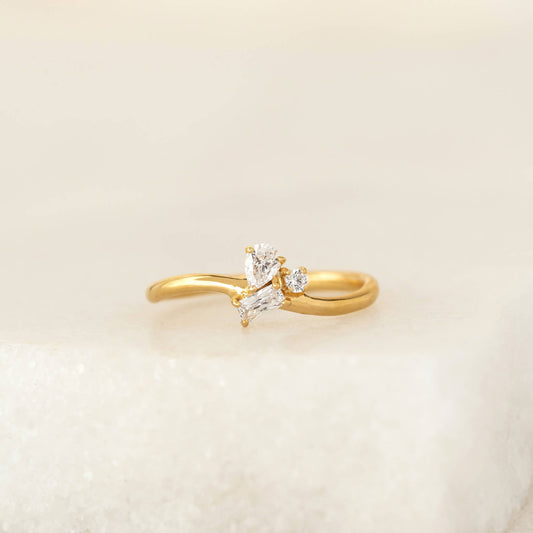 Delicate Gold Vermeil ring featuring a cluster of mixed-cut gemstone, including pear, round, and baguette shapes, set on a slim band and displayed on a soft neutral surface.