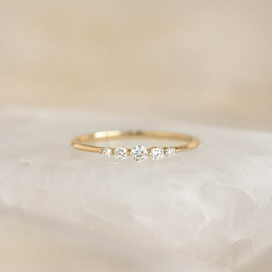 Close-up of Graduated Diamond Ring 14k Gold - Dahlia with five diamonds on a slim yellow gold band on a soft background