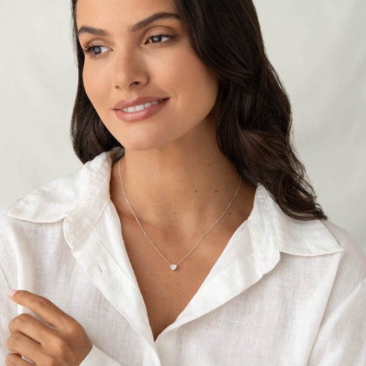 Woman in a white collared blouse wearing a delicate White Gold necklace with a heart-shaped gemstone pendant.