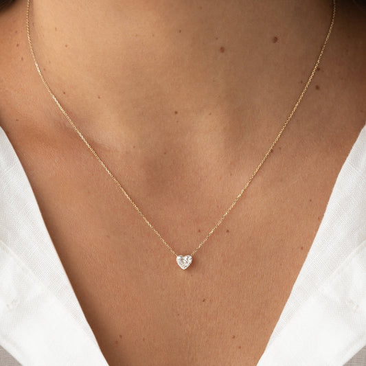 Close-up of a delicate Gold necklace featuring a heart-shaped gemstone pendant, worn with a white V-neck top.