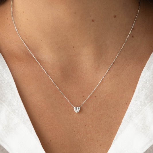 Close-up of a delicate White Gold necklace featuring a heart-shaped gemstone pendant, worn with a white V-neck top.