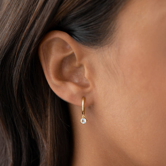 Close-up of ear wearing June Birthstone Drop Huggie Earrings - Moonstone with gold vermeil setting on a neutral background