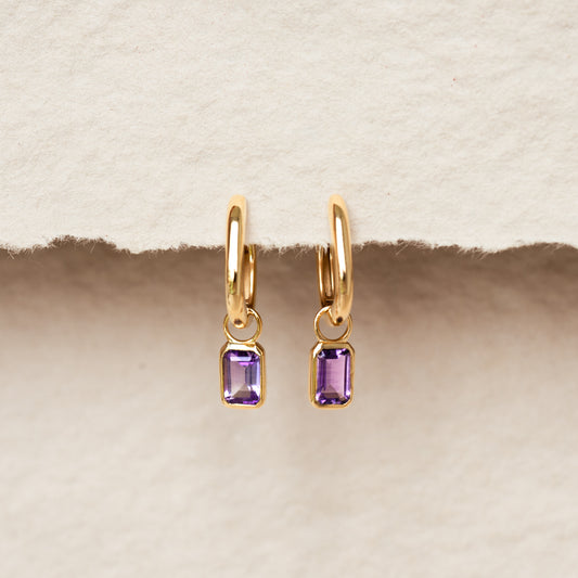 Huggie Earrings with Baguette Charms Amethyst - Amelia displayed on textured neutral background