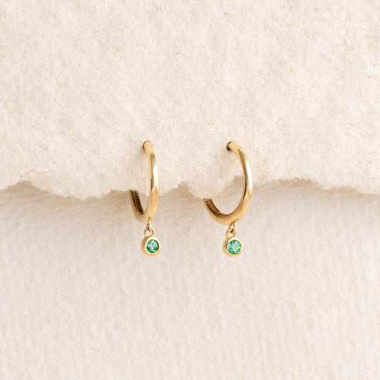 Emerald Huggie Earrings 14k Gold - Bianca with bezel-set emeralds hanging from polished gold hoops on a neutral background