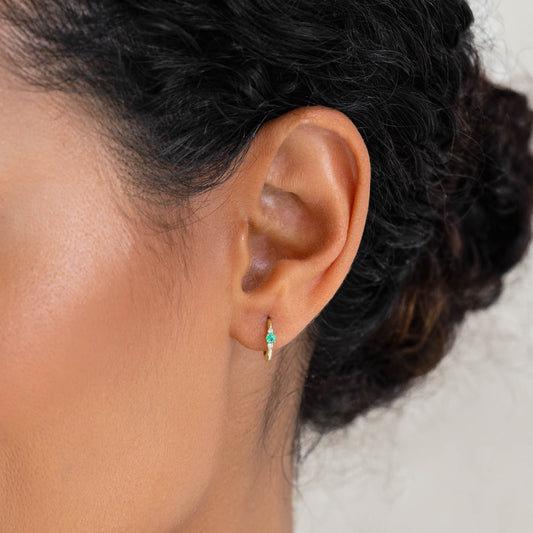 Close-up of a woman wearing Emerald Huggie Earrings 14k Gold - Etta with green emerald and diamond stones