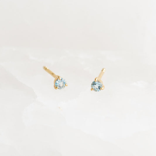 March Birthstone Stud Earrings 14k Gold - Blue Topaz set in delicate three-prong yellow gold settings on white background