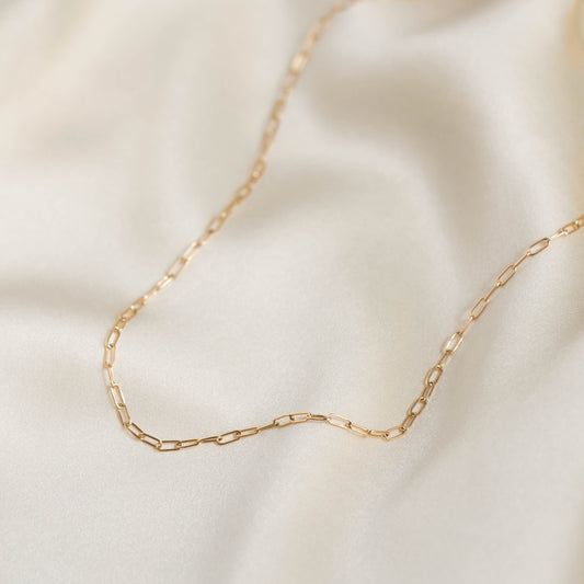 Close-up of a delicate Chain Link Necklace 14k Gold with paperclip links draped on soft beige fabric background