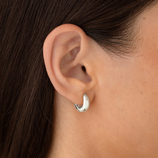 Close-up of a woman’s ear wearing Dome Huggie Earrings Silver - Caja with a smooth tapered dome shape in sterling silver