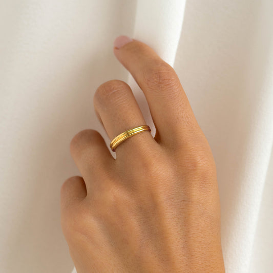 Close-up of a hand wearing the Double Stacking Ring - Idalia with a soft ribbed gold vermeil design on a neutral background