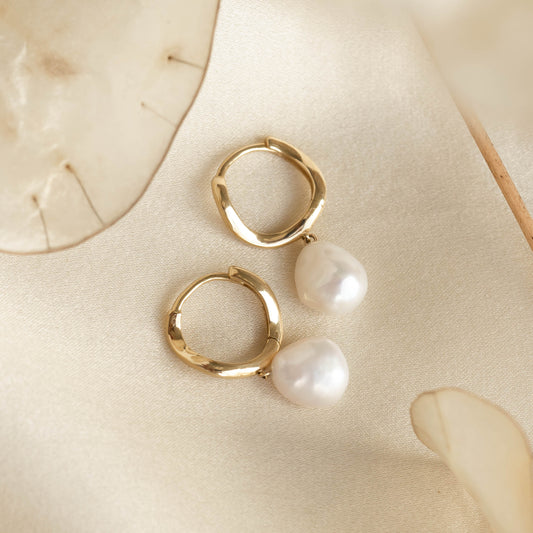Baroque Pearl Twist Huggie Earrings 14k Gold with wave-shaped hoops and freshwater baroque pearl drops on a soft cream background