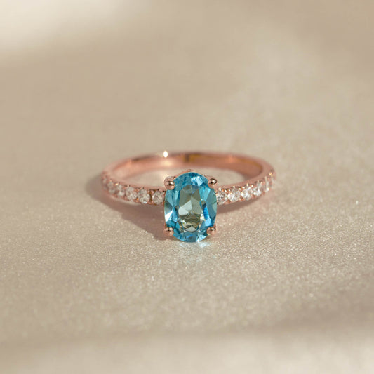 Oval Swiss Blue Topaz and Diamond Ring Rose Gold - Minette with pavé diamonds and a vibrant blue topaz stone on a soft neutral background