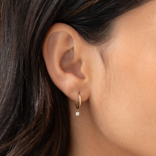 Close-up of an ear wearing Diamond Drop Huggie Earrings 14k Gold - Joleen with a small dangling diamond drop