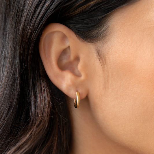 Close-up of a woman wearing Bold Huggie Earrings 14k Gold - Svea with smooth polished finish on a neutral background