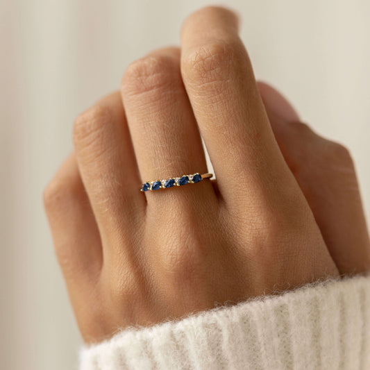 Close-up of a hand wearing the Sapphire Half Eternity Ring 14k Gold - Capriana with blue sapphires on a neutral background