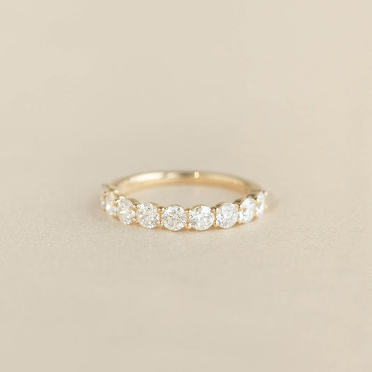 A delicate Yellow Gold ring featuring a row of round cut diamonds set along the band, displayed on a soft beige background.