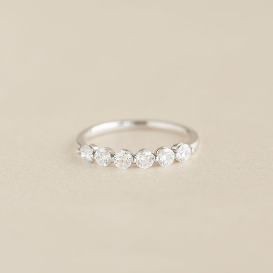 A delicate White Gold ring featuring a round diamonds set along the band, displayed on a soft beige background.