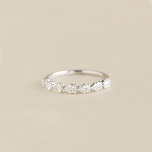 A delicate White Gold ring featuring a row of alternating pear cut diamonds set along the band, displayed on a soft beige background.