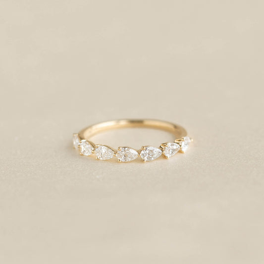 A delicate Yellow Gold ring featuring a row of alternating pear cut diamonds set along the band, displayed on a soft beige background.