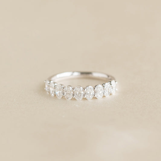 A delicate White Gold ring featuring a row of alternating oval cut diamonds set along the band, displayed on a soft beige background.