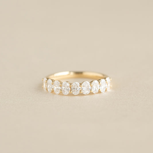 A delicate Yellow Gold ring featuring a row of alternating oval cut diamonds set along the band, displayed on a soft beige background.