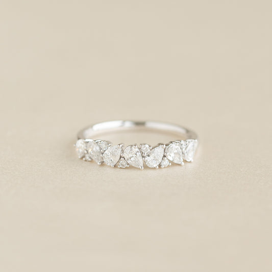 A delicate White Gold ring featuring a row of alternating pear-shaped and round diamonds set along the band, displayed on a soft beige background.