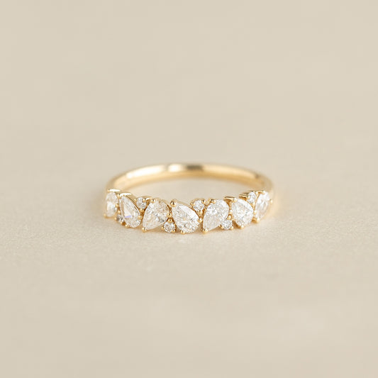 A delicate Yellow Gold ring featuring a row of alternating pear-shaped and round diamonds set along the band, displayed on a soft beige background.