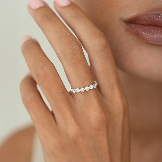 A close-up of a hand wearing a delicate White Gold ring set with round diamonds, styled on the ring finger against a soft neutral background.