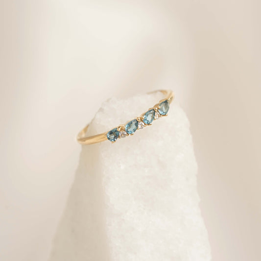 Close-up of September Birthstone Pear Ring 14k Gold - London Blue Topaz and Diamond on a white textured surface