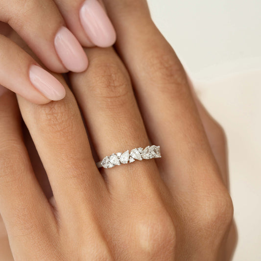 A close-up of a hand wearing a delicate White Gold ring set with alternating pear-shaped and round diamonds, styled on the ring finger against a soft neutral background.