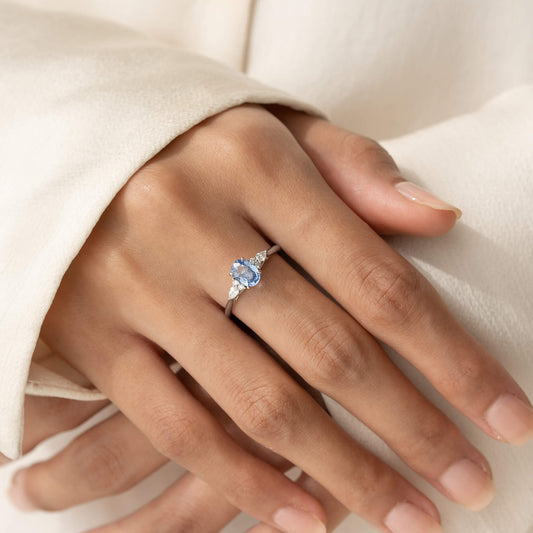 A close-up shot of a person's hand wearing the Alruna oval sapphire floral White Gold ring on their middle finger.