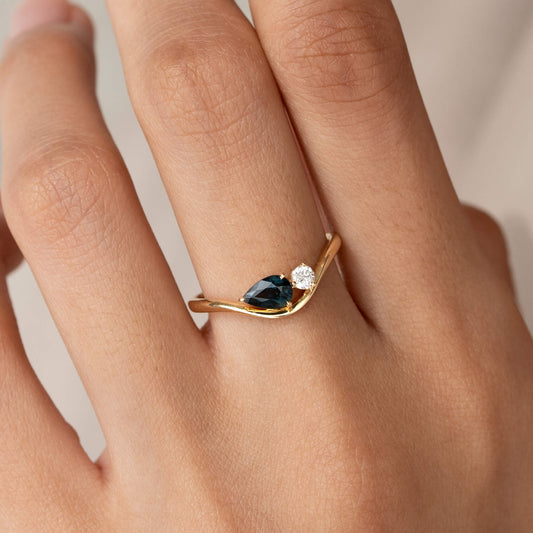 The photo focuses closely on the hand, offering a clear view of how the minimalist, modern Yellow Gold jewelry piece sits on the finger against a softly blurred, neutral background.