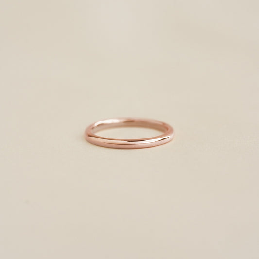 Close-up of a slim polished Round Rose Gold Band - Marni resting on a soft beige surface with subtle reflections