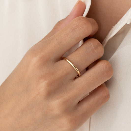 Close-up of a hand wearing the Round 14k Gold Band - Marni on the ring finger against a neutral background