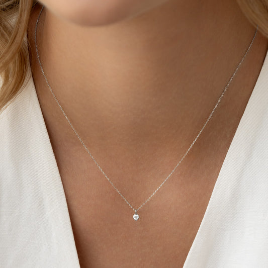 Close-up of a woman wearing the Diamond Pendant Necklace White Gold - Atiana with a single round diamond on a delicate chain