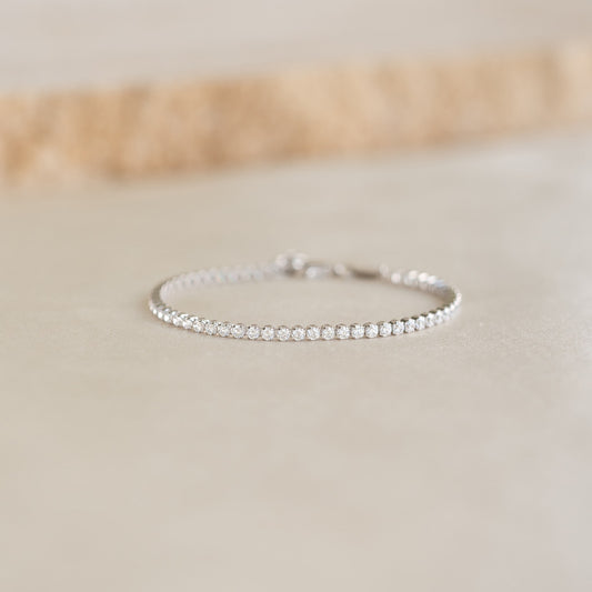 Close-up of Tennis Bracelet Silver - Audrey featuring sparkling cubic zirconia stones on a sterling silver chain resting on a beige surface