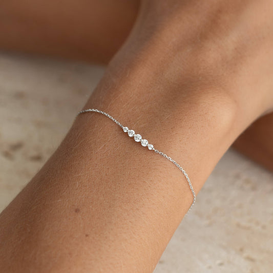 Close-up of a wrist wearing Graduated Diamond Bracelet White Gold - Tamsin with five graduated diamonds on a delicate chain